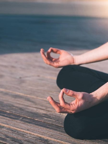 Detail of the hands of a young man who meditates practicing yoga on some wooden boards in the lotus position.